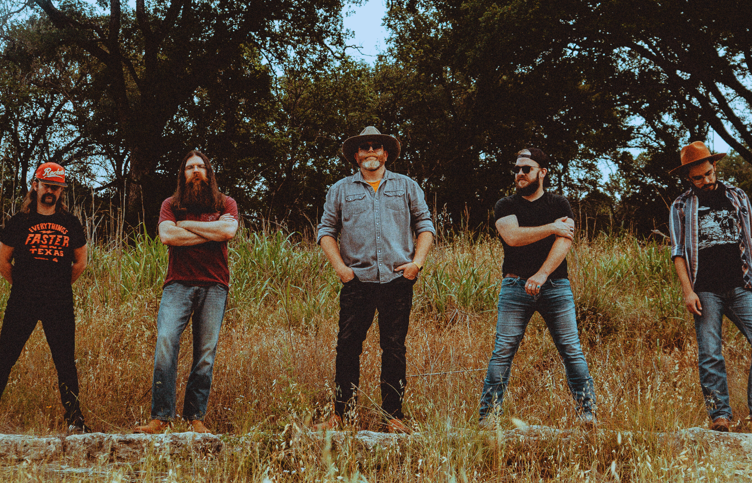 Band standing in front of large bushes and trees